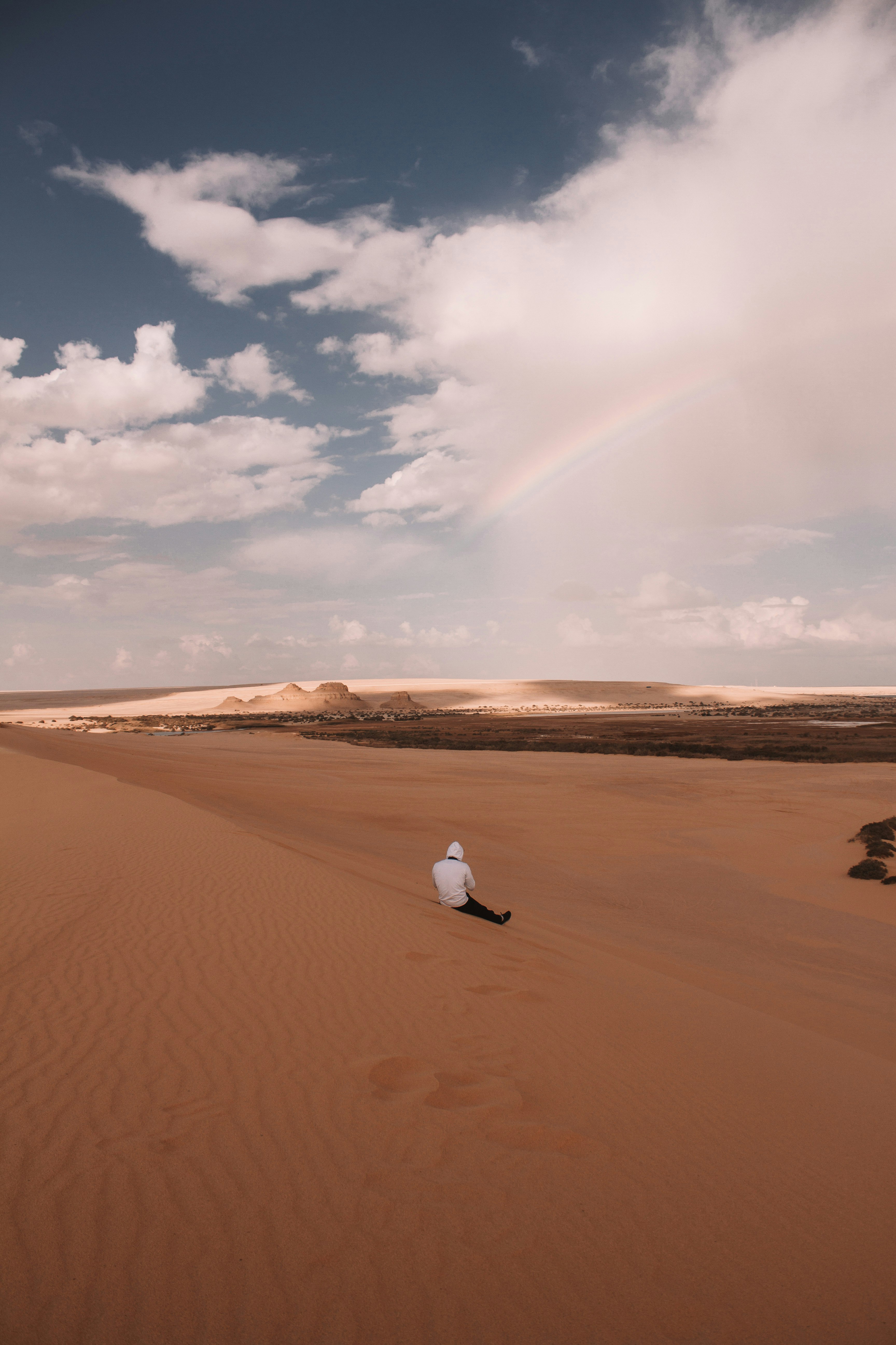 person in white shirt walking on brown sand under white clouds during daytime